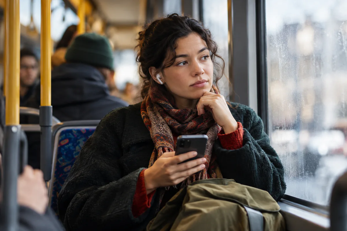 A traveler wearing earphones holds a phone while seated on a train.