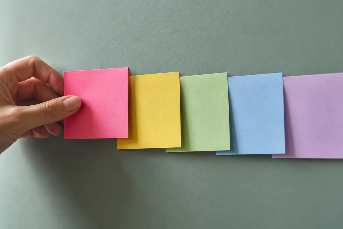 A hand places a new note beside an overlapping sequence of colored cards.